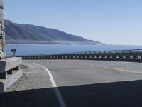 an empty road going through front of mountains on the ocean side with mountains in the background