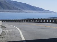 an empty road going through front of mountains on the ocean side with mountains in the background