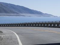 an empty road going through front of mountains on the ocean side with mountains in the background