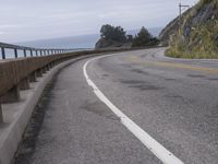 an empty road on a cliff side next to the ocean and shore line near some rock cliffs