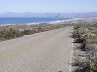 an empty road with two lanes stretching along a shoreline in front of the ocean and mountains