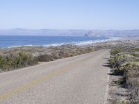 an empty road with two lanes stretching along a shoreline in front of the ocean and mountains