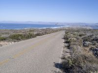 an empty road with two lanes stretching along a shoreline in front of the ocean and mountains