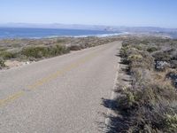 an empty road with two lanes stretching along a shoreline in front of the ocean and mountains