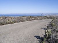 an empty road with two lanes stretching along a shoreline in front of the ocean and mountains