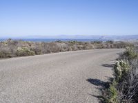 an empty road with two lanes stretching along a shoreline in front of the ocean and mountains