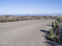 an empty road with two lanes stretching along a shoreline in front of the ocean and mountains