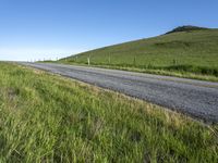 an empty road with a single lane through tall grass and a hill on the other side