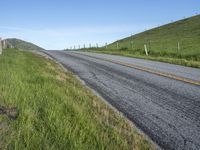 an empty road with a single lane through tall grass and a hill on the other side