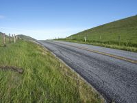 an empty road with a single lane through tall grass and a hill on the other side