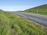 an empty road with a single lane through tall grass and a hill on the other side