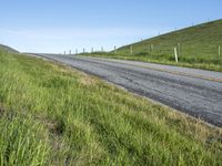 an empty road with a single lane through tall grass and a hill on the other side