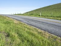 an empty road with a single lane through tall grass and a hill on the other side