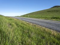 an empty road with a single lane through tall grass and a hill on the other side