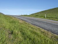 an empty road with a single lane through tall grass and a hill on the other side