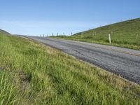 an empty road with a single lane through tall grass and a hill on the other side