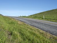 an empty road with a single lane through tall grass and a hill on the other side