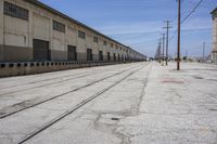 there is a road with two train tracks that are going through an industrial building in the distance, and there are trees on the right side