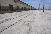 there is a road with two train tracks that are going through an industrial building in the distance, and there are trees on the right side