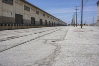 there is a road with two train tracks that are going through an industrial building in the distance, and there are trees on the right side