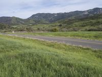 a motorcycle is riding along a mountain road in the distance, with grassy hillsides