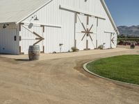 the large white barn is surrounded by two wine barrels and grass around it on the outside of the barn