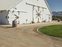 the large white barn is surrounded by two wine barrels and grass around it on the outside of the barn