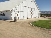 the large white barn is surrounded by two wine barrels and grass around it on the outside of the barn