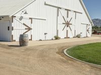 the large white barn is surrounded by two wine barrels and grass around it on the outside of the barn