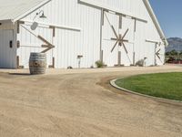 the large white barn is surrounded by two wine barrels and grass around it on the outside of the barn