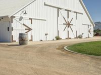 the large white barn is surrounded by two wine barrels and grass around it on the outside of the barn