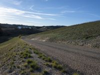 a dirt road winding into a small hill side village surrounded by grass, shrubs and blue sky