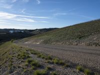 a dirt road winding into a small hill side village surrounded by grass, shrubs and blue sky