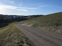 a dirt road winding into a small hill side village surrounded by grass, shrubs and blue sky