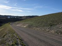 a dirt road winding into a small hill side village surrounded by grass, shrubs and blue sky