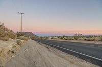 the road has some cracks on it near the stop sign and telephone pole in the desert