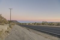 the road has some cracks on it near the stop sign and telephone pole in the desert