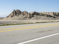 a road with yellow lines leads to desert and mountains behind them as a bike rider rides on an empty road