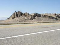 a road with yellow lines leads to desert and mountains behind them as a bike rider rides on an empty road