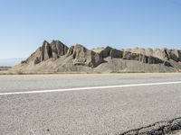 a road with yellow lines leads to desert and mountains behind them as a bike rider rides on an empty road