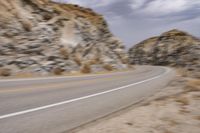 a motorcycle traveling down a street next to a mountain side of a cliff and an empty road in the middle