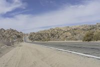 a road with gravel and small bushes on each side of it and a hill in the background