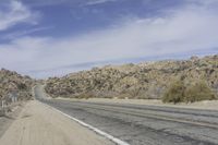 a road with gravel and small bushes on each side of it and a hill in the background