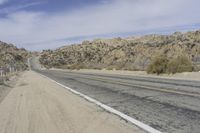 a road with gravel and small bushes on each side of it and a hill in the background