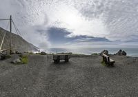 benches on the side of the road with an ocean in the background and mountains below