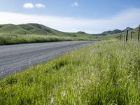 a car sits on the roadside beside a field of grass with hills and valleys behind it