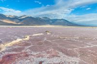 a rocky body of water near mountains and rocks in a vast area, with purple and green colors