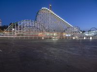 the empty amusement park with some roller coasters going by it at night - -