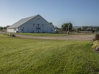 a white barn on a grassy lot with a bike and grass trail near it in the foreground