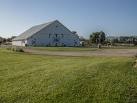 a white barn on a grassy lot with a bike and grass trail near it in the foreground